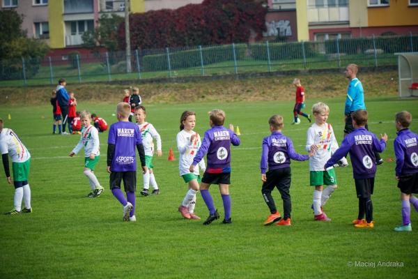 Dzieci w fioletowych koszulkach Narew Choroszcz witają się z zawodnikami w biało-zielonych strojach na boisku przed meczem żaków U9.